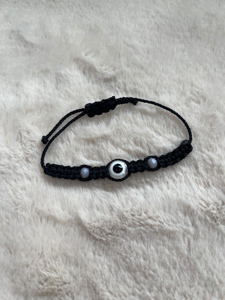 a black cord bracelet with an evil eye beaded on it, sitting on a white furnishing