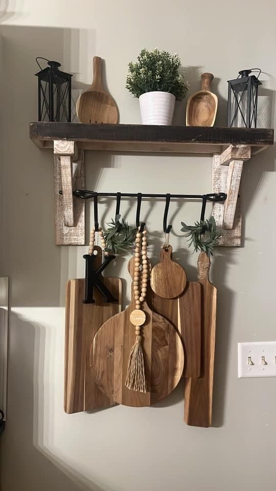 wooden utensils and cutting boards are hanging on a wall above a shelf with potted plants