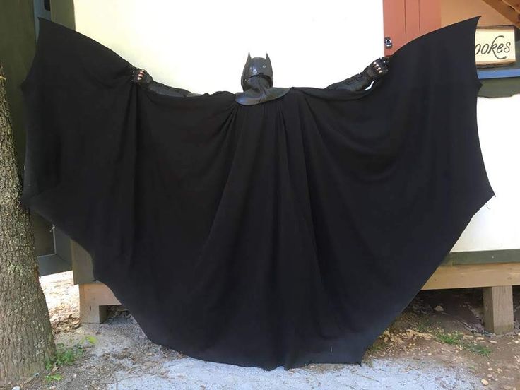 a black bat hanging on the side of a building next to a tree and fence