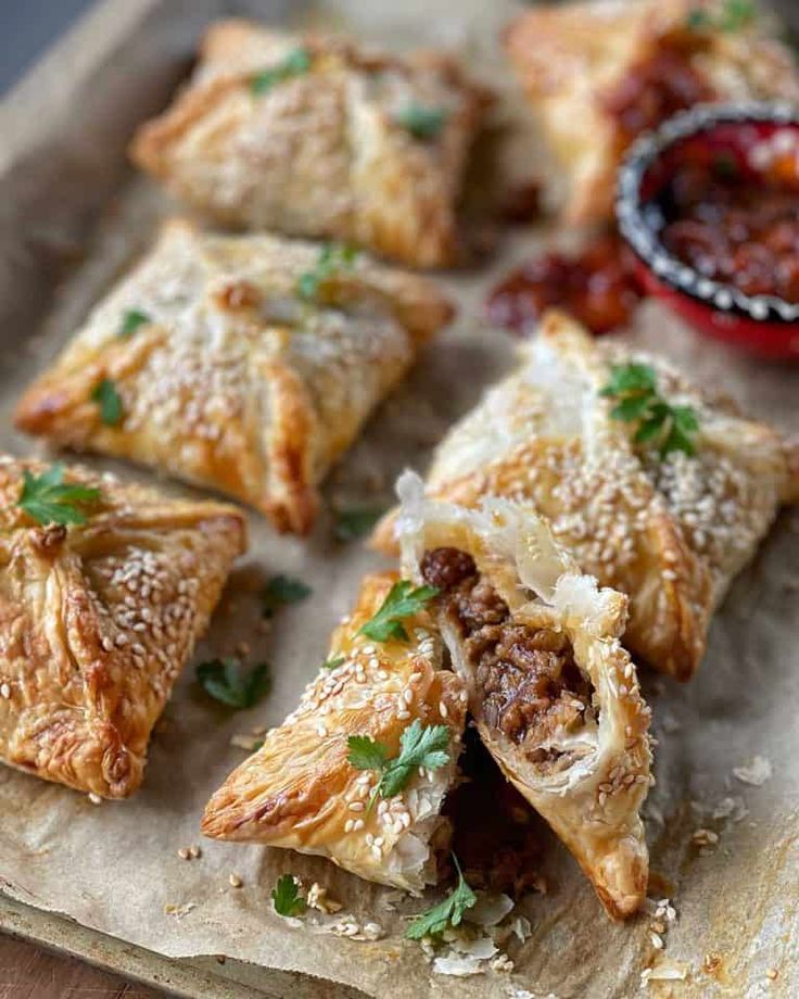 several pastries with meat and cheese on a piece of parchment paper next to dipping sauce