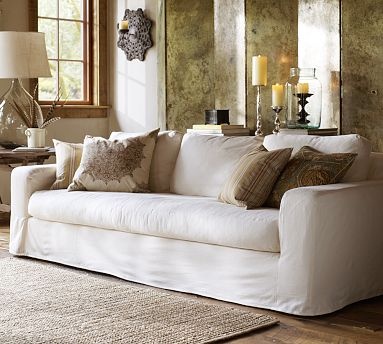 a living room filled with white furniture and lots of pillows on top of a rug