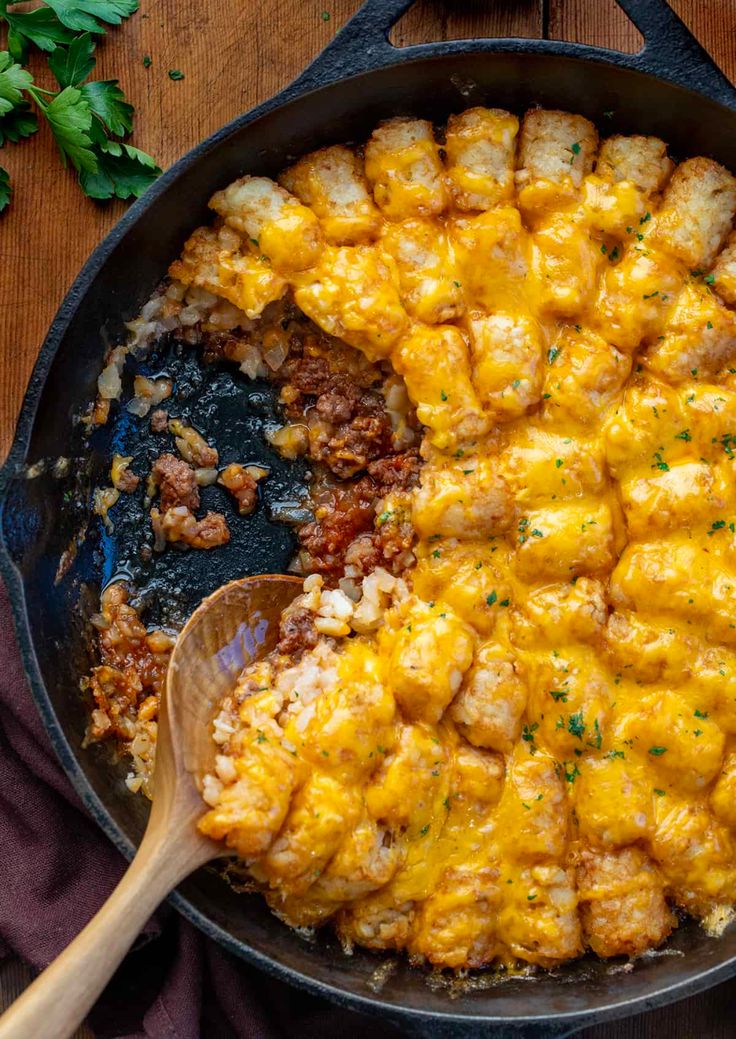 a skillet filled with tater tots covered in cheese and meat next to a wooden spoon