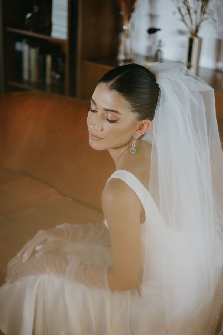 a woman in a white dress sitting on a couch wearing a veil and diamond earrings