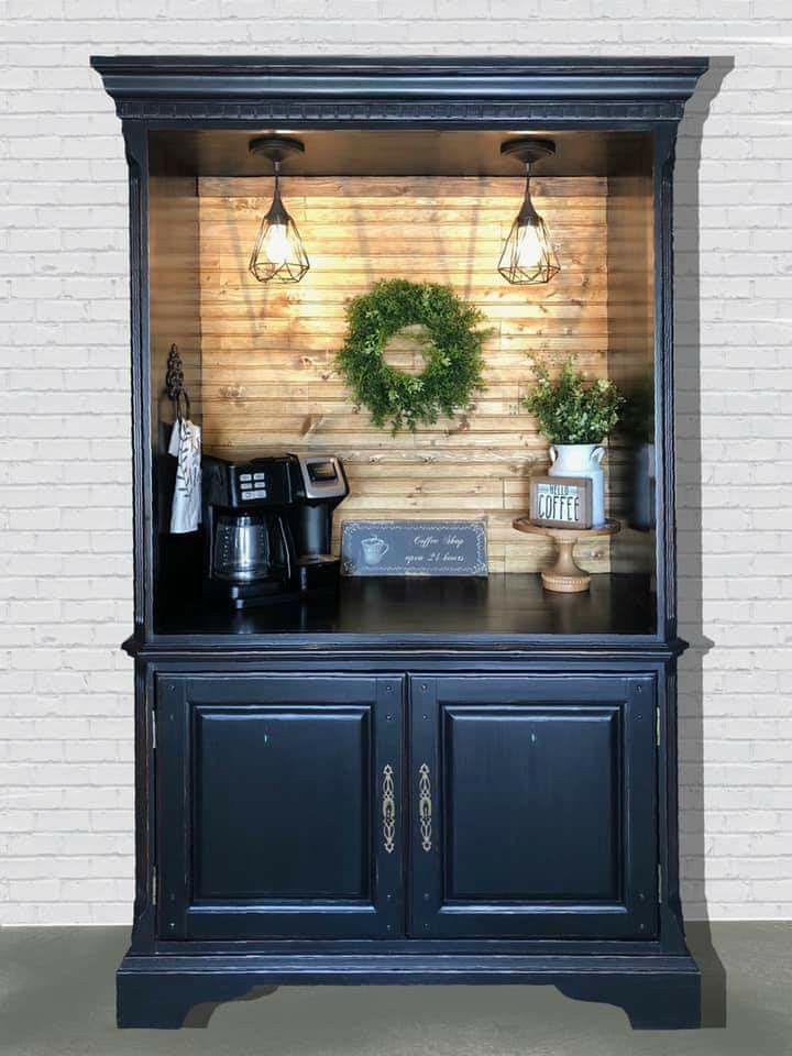 an old fashioned black china cabinet with plants and coffee maker on top in front of a white brick wall