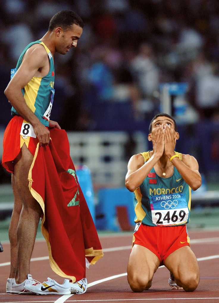 a man wiping his face while sitting on the ground next to another man who is covering his eyes