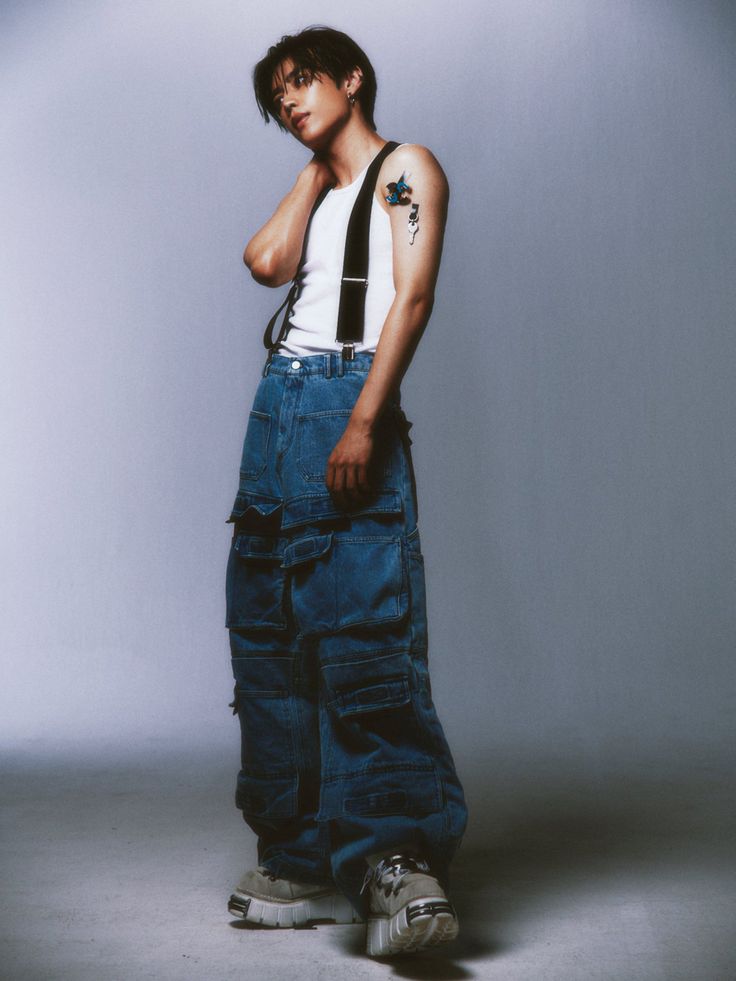 a young man in overalls is posing for the camera with his hand on his chin