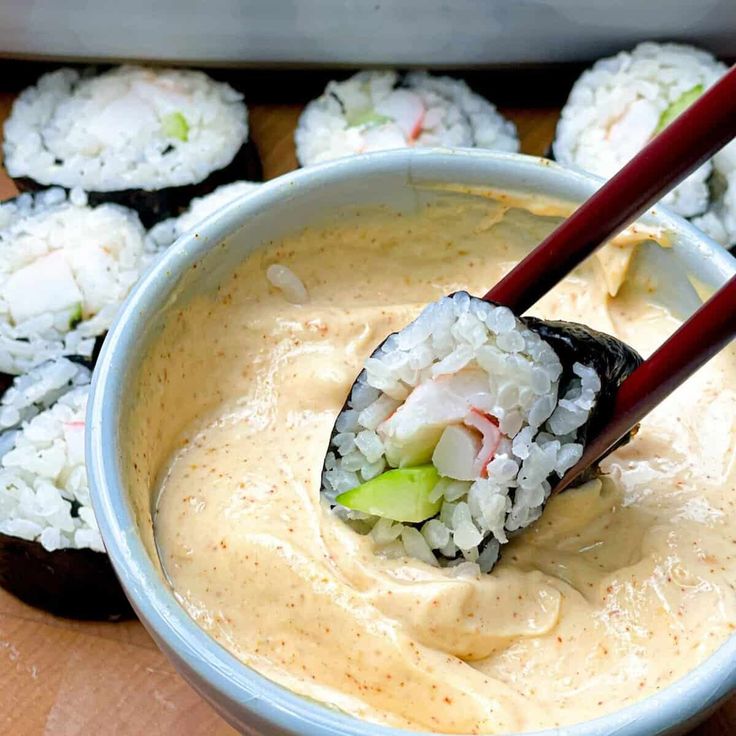 sushi being dipped with chopsticks in a bowl filled with rice and sauce