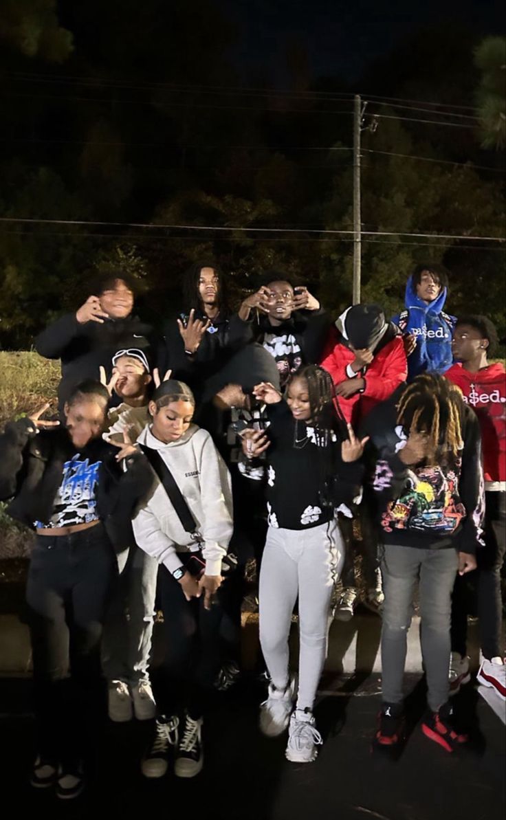 a group of people standing next to each other on a street at night with their hands in the air