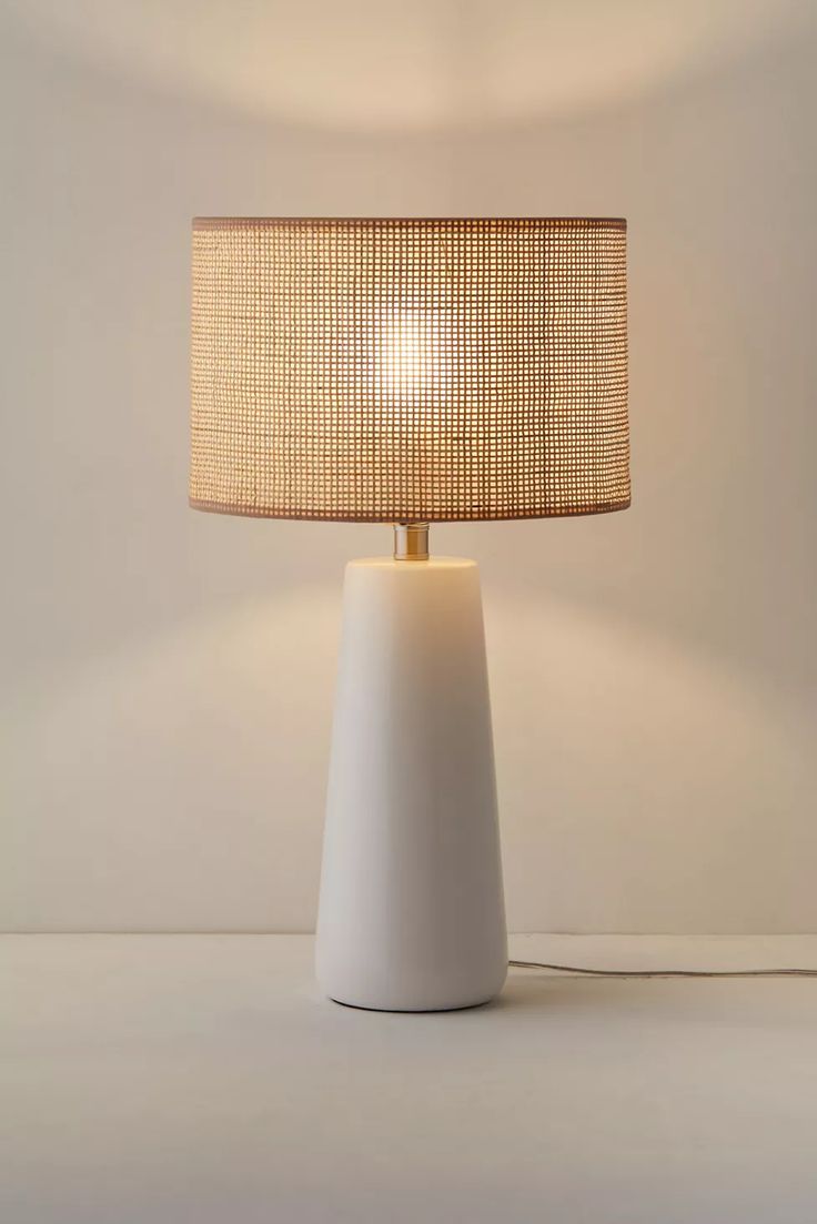 a white table lamp with a beige shade on it's base and a light bulb in the middle