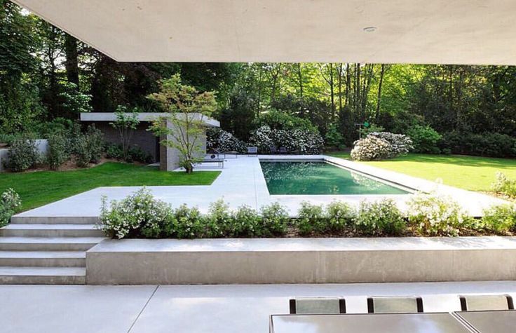 an outdoor swimming pool surrounded by greenery and trees in the back yard with steps leading up to it