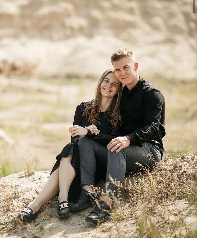 a man and woman sitting on top of a sandy hill