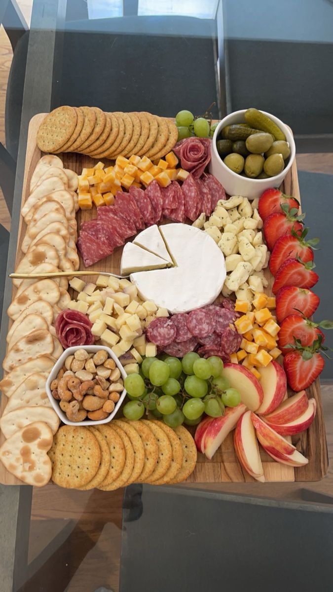 an assortment of cheeses, crackers and fruit on a wooden platter