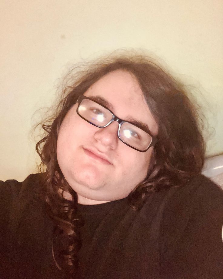 a person with long hair and glasses laying down on a bed looking at the camera