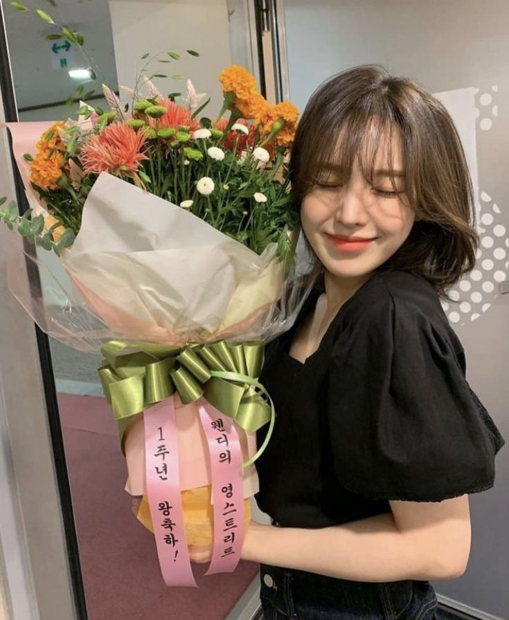 a woman holding a bouquet of flowers in front of a glass door with writing on it