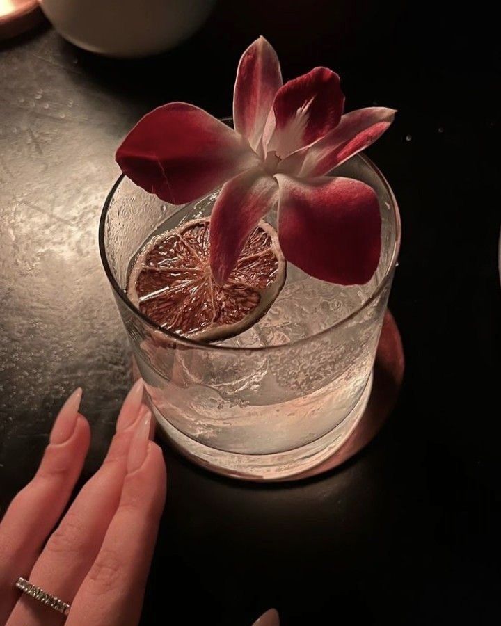 a close up of a person's hand near a glass with a flower in it