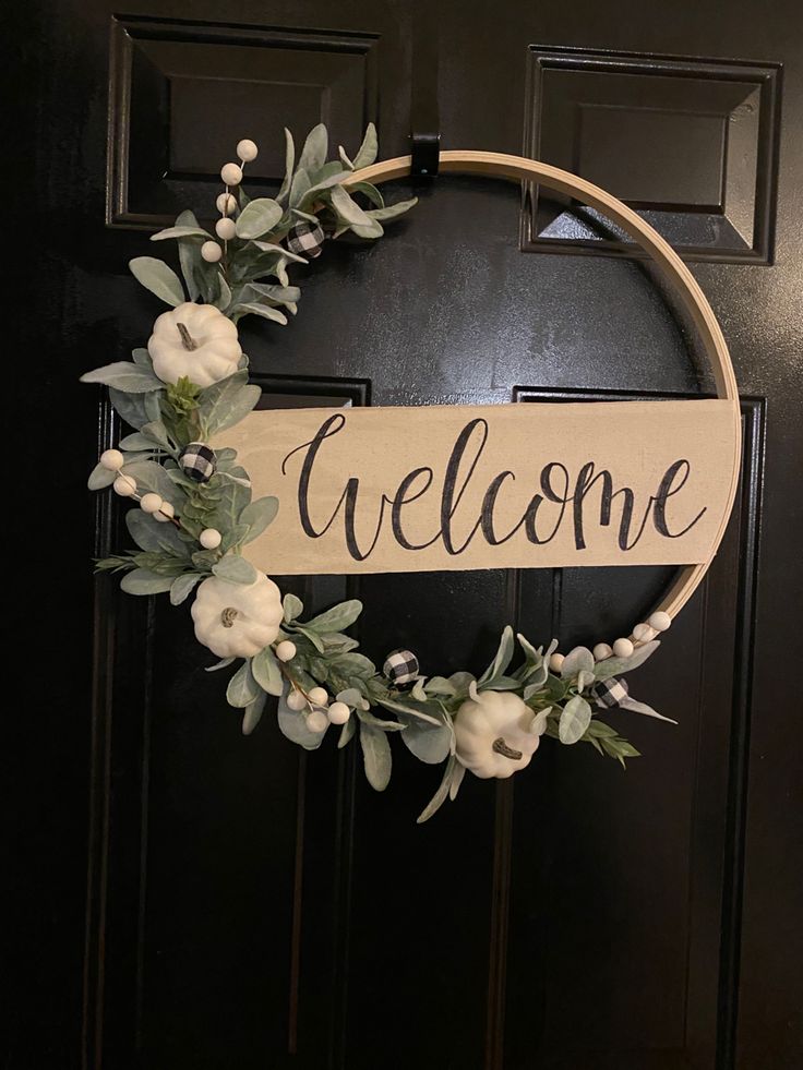 a welcome sign hanging on the front door with flowers and greenery around it's edges