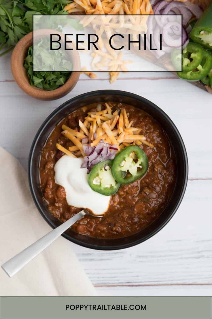 a bowl filled with chili and cheese on top of a white table next to other food