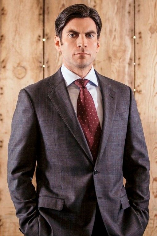 a man wearing a suit and tie standing in front of a wooden wall with lights