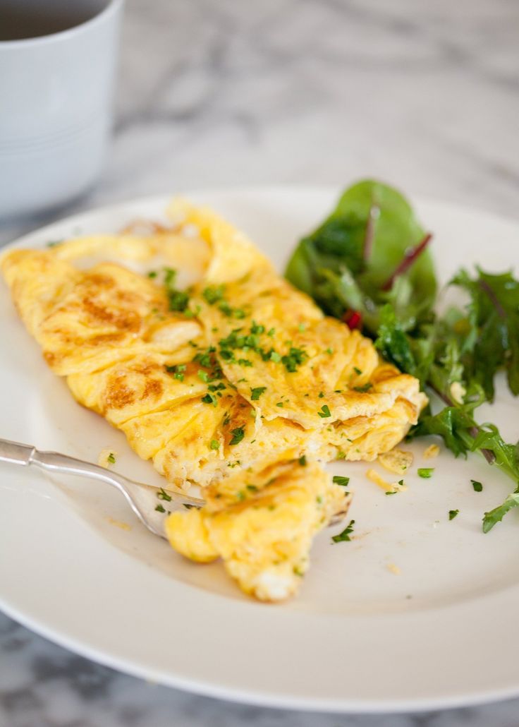 an omelet on a plate with a side of greens and a cup of coffee