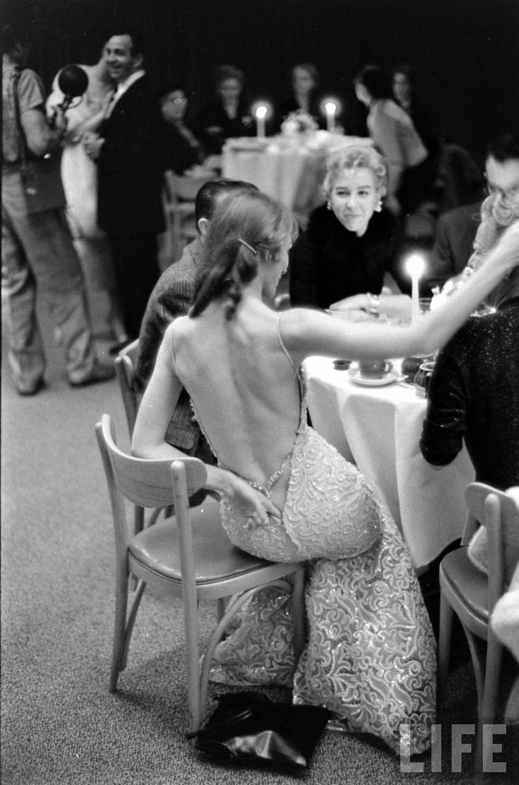 a woman in a dress sitting at a table with other people around her and candles on the table