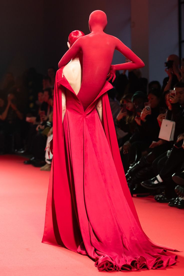 a woman in a red dress walking down a runway with her back turned to the camera