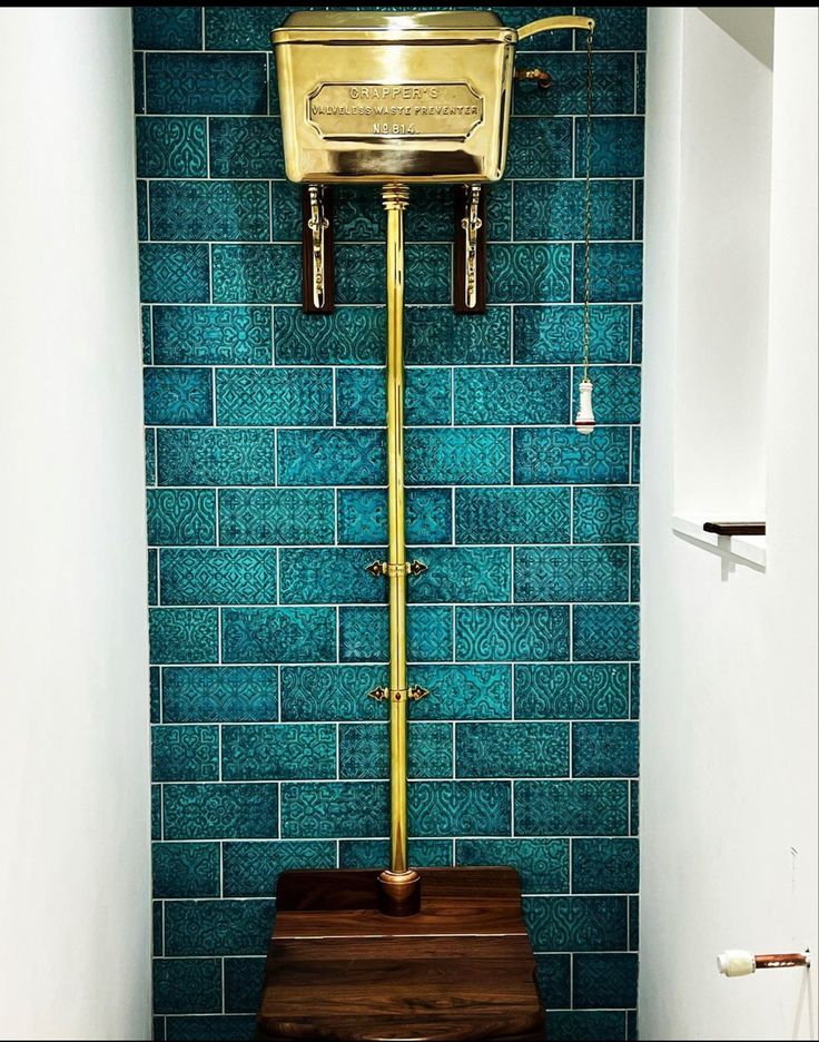 a toilet in a bathroom with blue tiles and gold fixtures on the tank cover above it