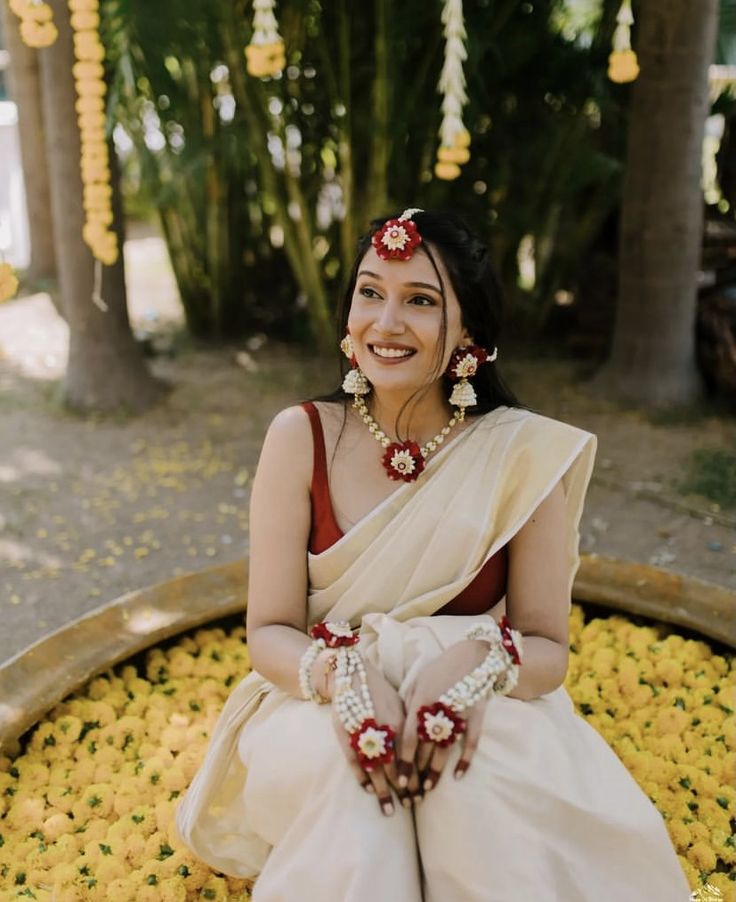 a woman sitting on top of a flower filled field wearing a white and red sari