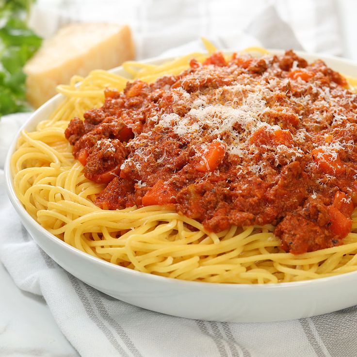 a plate of spaghetti with meat sauce and parmesan cheese on the side next to bread