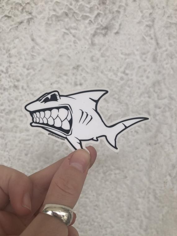 a hand holding up a sticker with a shark on it's face and teeth