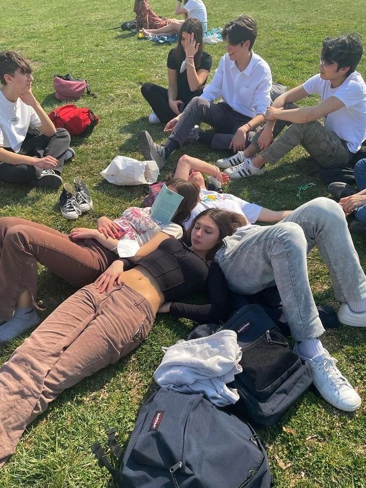 a group of young people sitting on top of a grass covered field next to each other