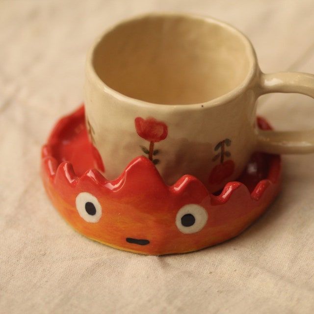 a ceramic cup and saucer with an animal face on the inside, sitting on a table cloth