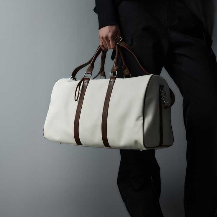 The Modern Canvas Duffle Bag effortlessly blends contemporary style with superior craftsmanship, making it a must-have for both travel and everyday use. Constructed from premium cotton canvas, this bag features PU leather accents that add a touch of sophistication and durability. The base of the bag is reinforced with four rivets, providing extra protection against wear and tear and extending its lifespan. Designed for versatility, it includes a detachable strap, allowing you to carry it as a cr Luxury Canvas Duffle Bag Functional Style, Modern Everyday Duffle Bag With Leather Backing, Elegant Leather Trim Travel Bag For Weekend Trips, Classic White Large Capacity Satchel, White Rectangular Weekender Bag For Everyday, White Large Capacity Bags For Weekend Trips, Elegant Travel Bag With Leather Trim For Weekend Trips, Modern Weekender Bag With Leather Backing, Elegant Canvas Travel Bag With Leather Handles