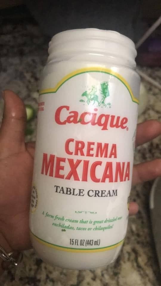 a hand holding a jar of cacique crema mexican table cream on a counter