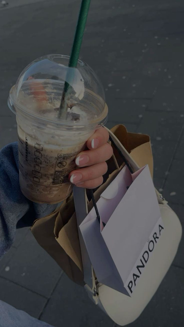 a person holding a starbucks drink in their hand with a paper bag on the other side