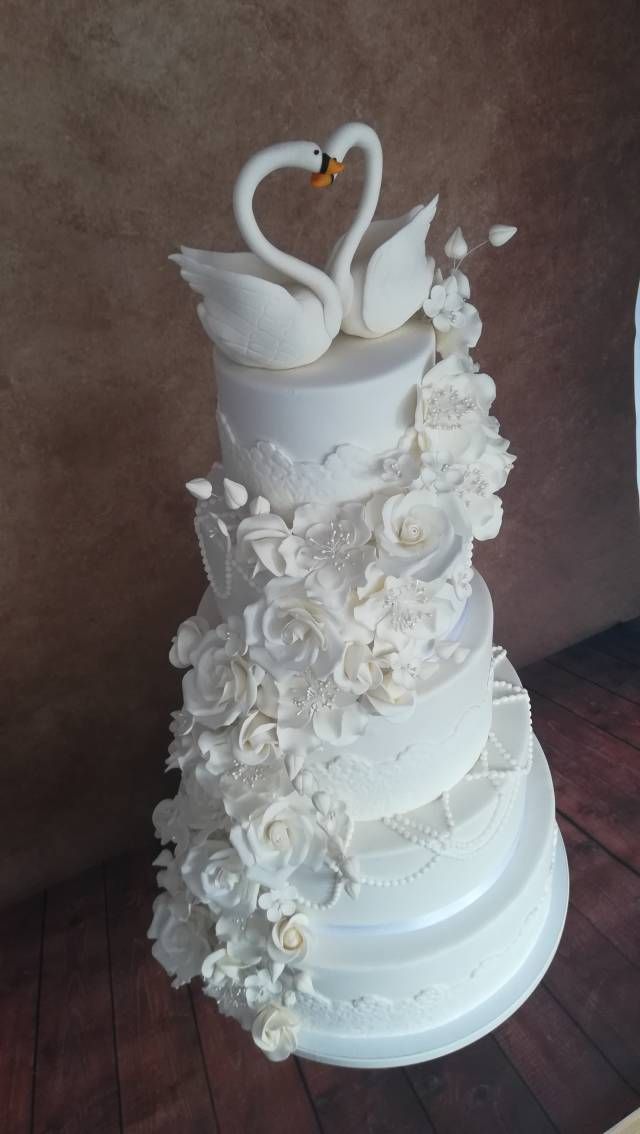 a three tiered wedding cake with white flowers and two swans on the top layer