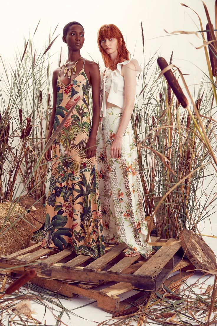 two women standing next to each other in front of tall grass and reeds,