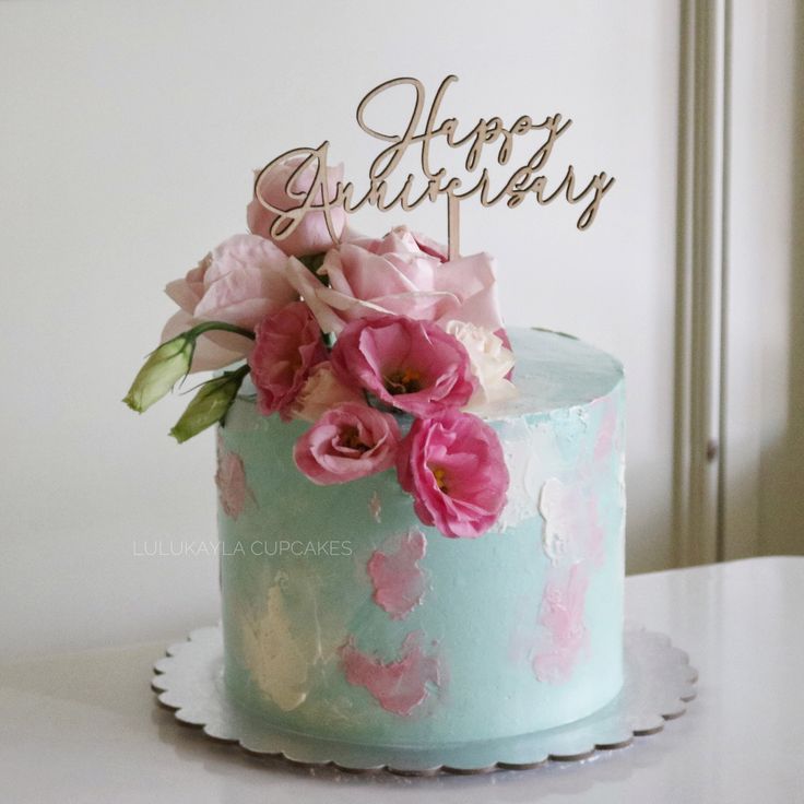 a blue cake with pink flowers on top and a happy birthday sign in the middle