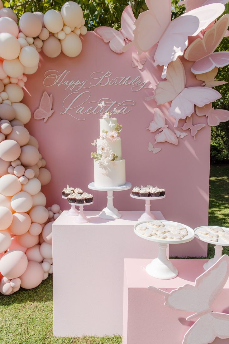 a cake and cupcakes on a table in front of a backdrop with balloons