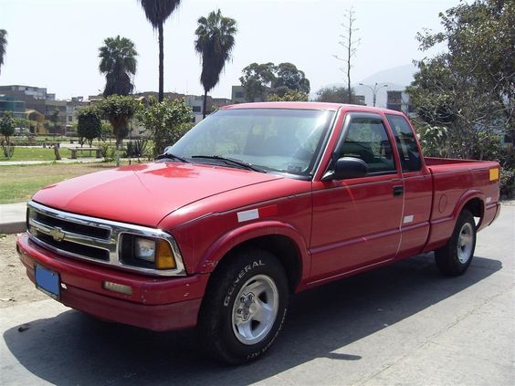 a red pick up truck parked on the side of the road in front of palm trees