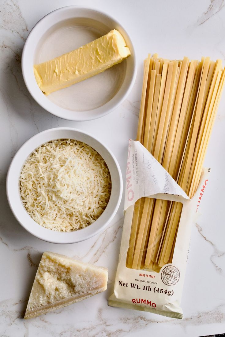 pasta, cheese and butter on a marble countertop with two bowls full of spaghetti