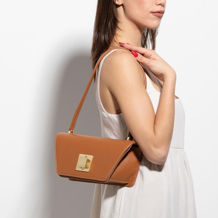 The Arcadia Trapeze combines geometric lines and an oversized front turn lock to create a contemporary style yet chic. A desing that stands out and matches perfectly with evening outfits. Elegant Workwear Bag With Fold Over Clasp, Timeless Evening Shoulder Bag With Hasp Closure, Modern Office Clutch With Removable Pouch, Modern Evening Flap Bag With Removable Pouch, Modern Brown Evening Bag With Removable Pouch, Modern Brown Flap Bag For Evening, Modern Brown Evening Shoulder Bag, Modern Flap Bag With Gold-tone Hardware For Work, Modern Flap Bag With Detachable Handle For Office