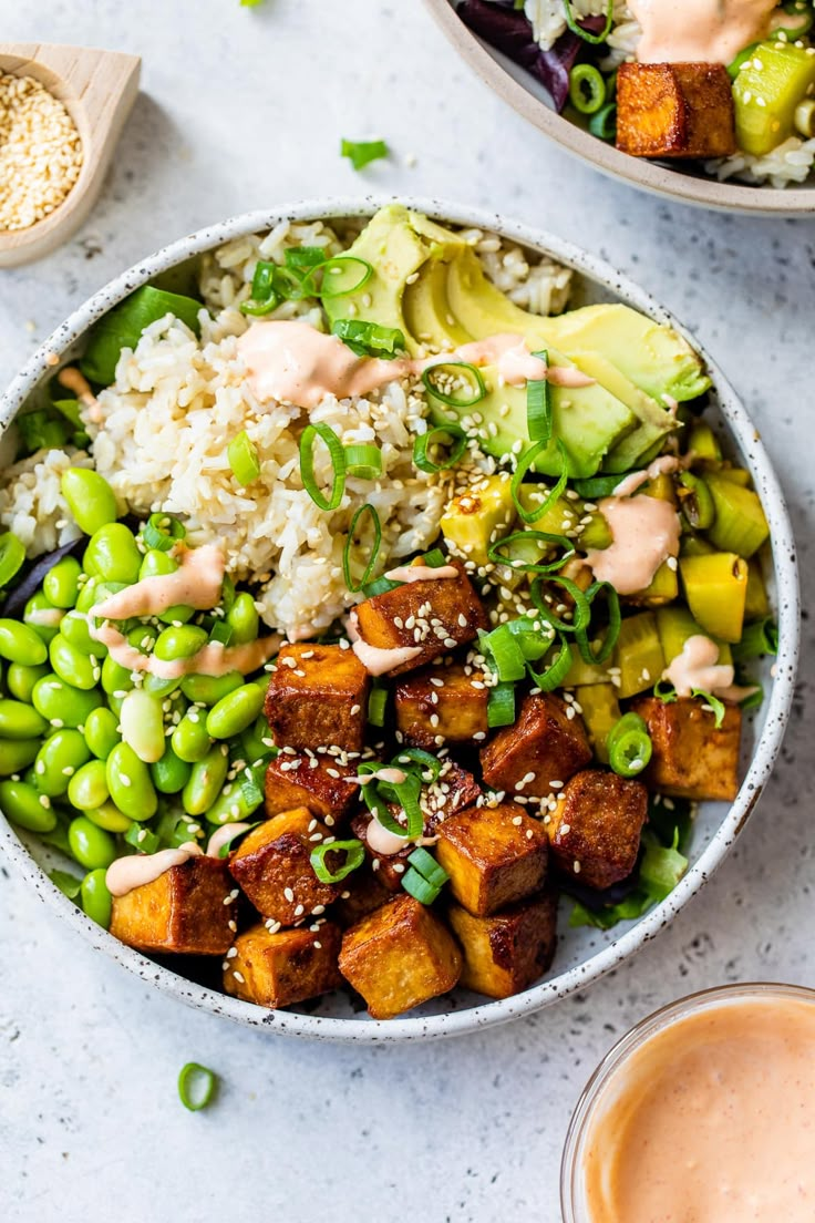 two bowls filled with rice, peas and tofu on top of a white table