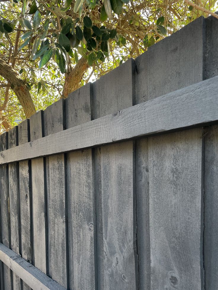 a wooden fence is shown in front of a tree and some leaves on the ground