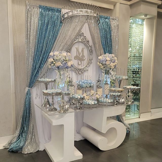 a white table topped with lots of vases filled with blue and white flowers next to a clock