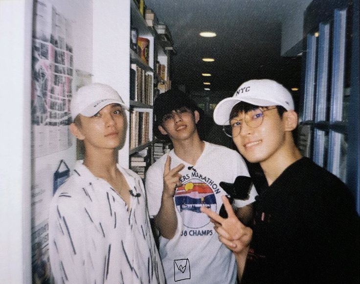 three young men standing next to each other in front of a book shelf with books on it