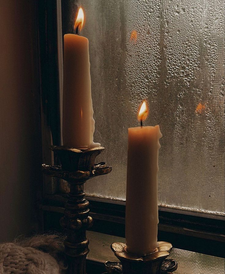 two lit candles sitting next to each other in front of a window covered with condensation