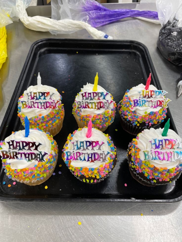 birthday cupcakes with white frosting and colorful sprinkles on a black tray