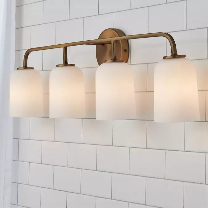 a bathroom light fixture with five lights on it's side and a white brick wall in the background