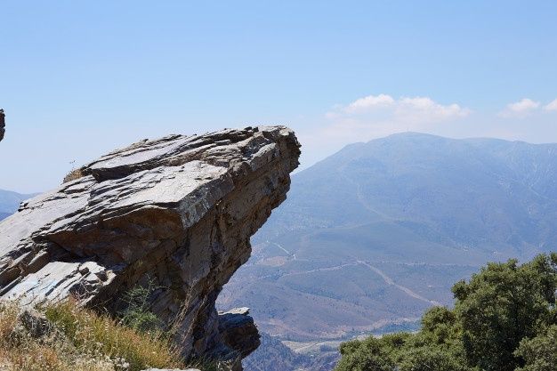 a man standing on top of a rock next to a lush green hillside