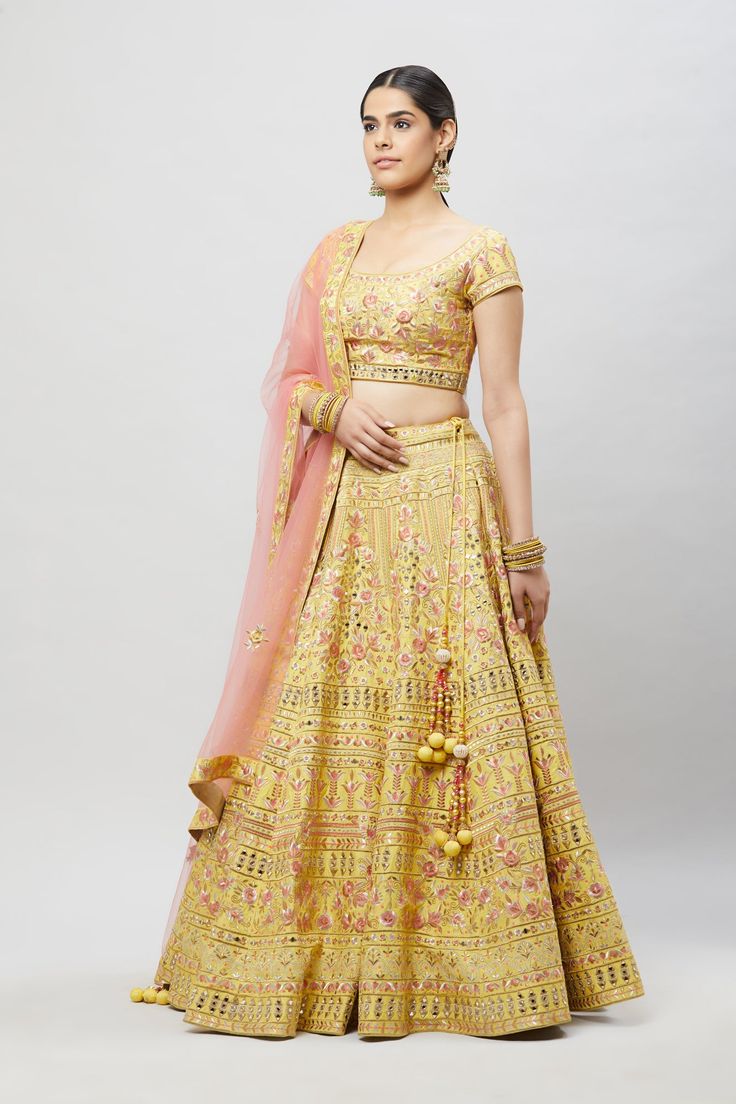 Beautifully embroidered with gold aari, pink resham and silver mirror embroidery, this lehenga will brighten up any wedding event! Fabric: Raw silk blouse and lehenga, Net dupatta All preorders will be handled by a Nazranaa Bridal Consultant who will virtually discuss measurements and minor changes according to the client's specifications Occasion: Wedding Events such as sangeet or wedding ceremony WASH CARE INSTRUCTIONS - Please Dry clean only when it is applicable. Slight color variation is po Festive Reception Choli With Gota Work, Reception Semi-stitched Gota Work Choli, Kundan Choli With Gota Work For Eid, Festive Kundan Lehenga With Cutdana Details, Festive Kundan Lehenga With Cutdana, Navratri Choli With Gota Work And Kundan Material, Chanderi Lehenga With Mirror Work For Reception, Semi-stitched Chanderi Lehenga With Gota Work, Gold Lehenga With Mirror Work In Art Silk